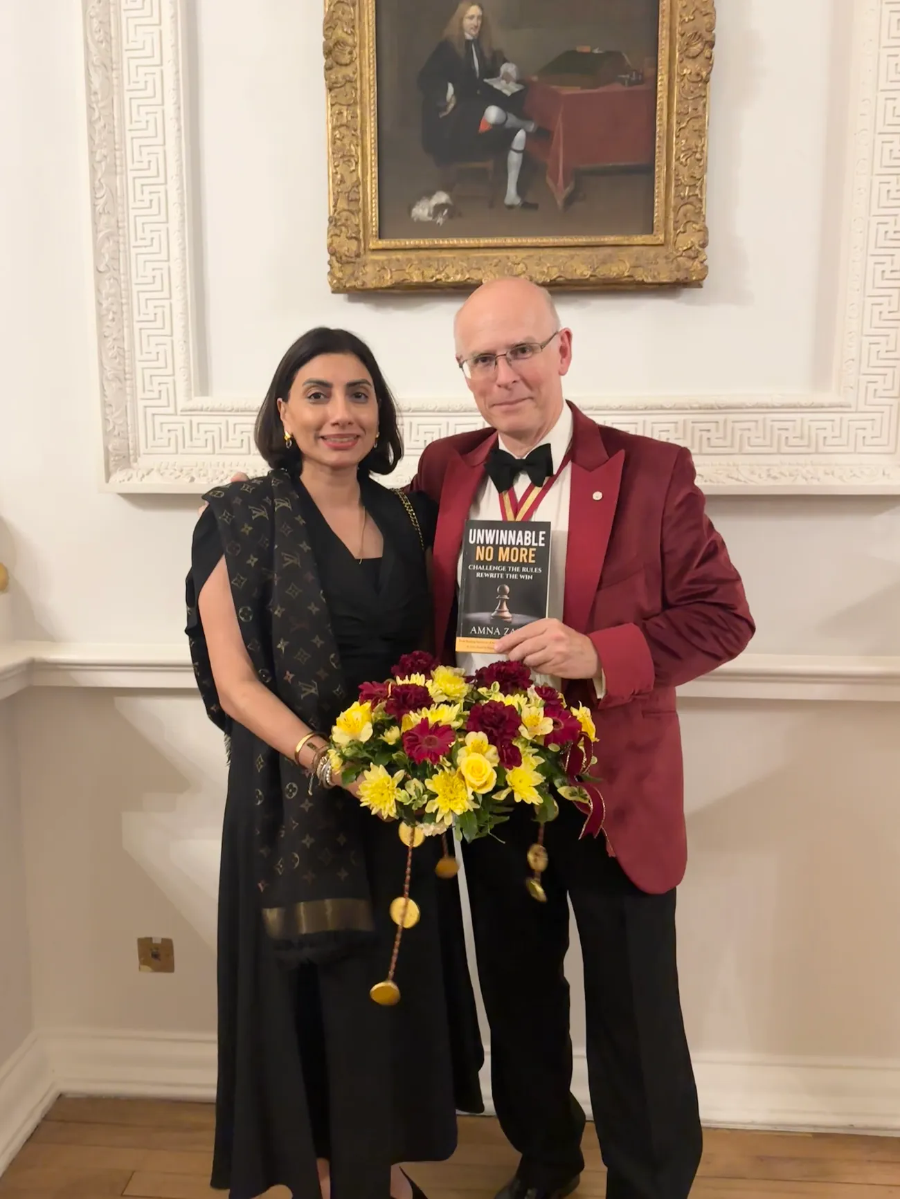 Amna Zaidi holding flowers beside a guest presenting a copy of Unwinnable No More